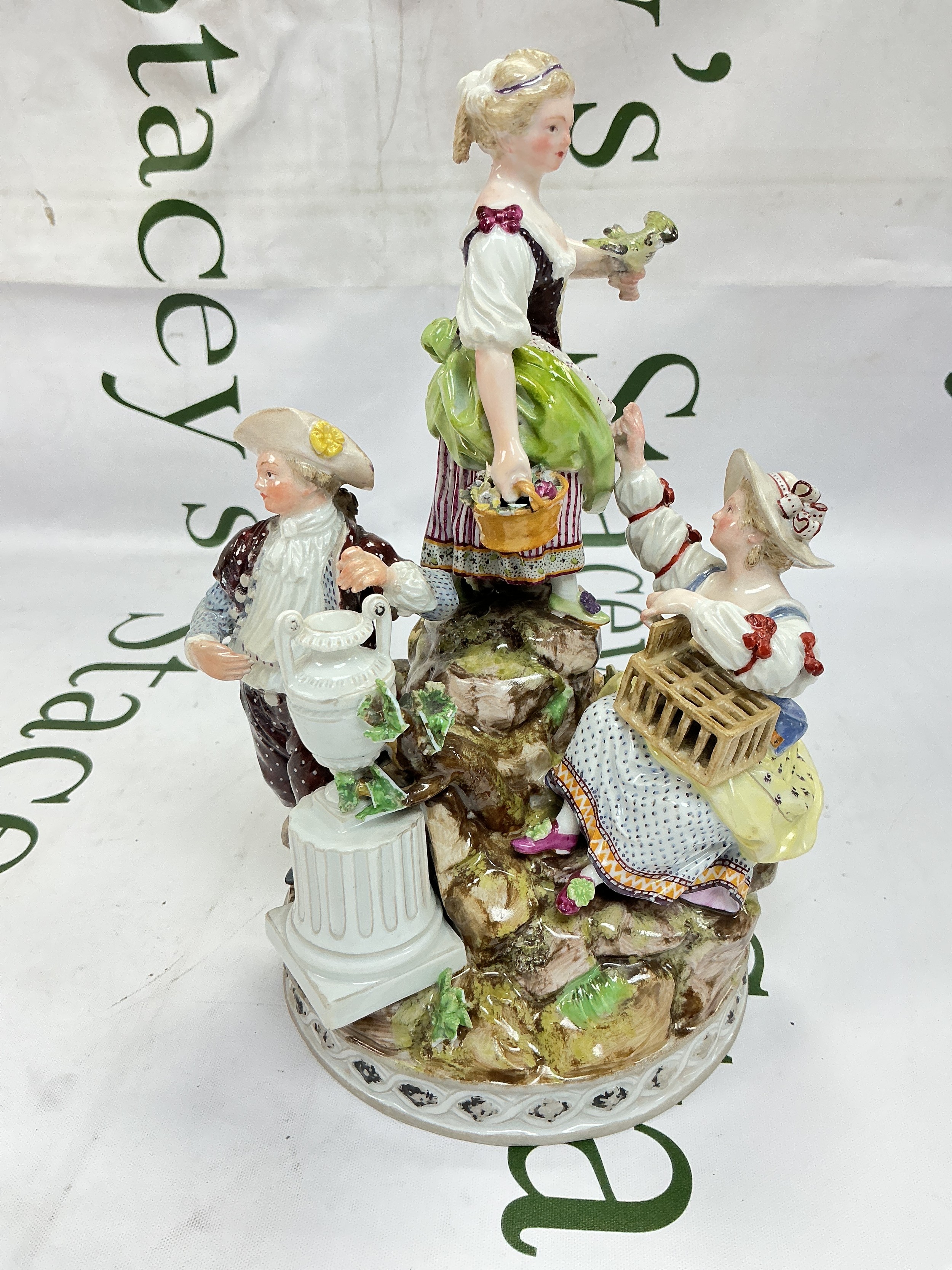 A 19th Century Meissen allegorical figure group, depicting Liberty and Matrimony, with three children around a rocky base, one holding a bird on her left hand, a girl beside her with a bird cage and a boy standing beside a tall vase, some chips and restoration. Blue swords mark and incised F94 to base. Approx height 22cm.