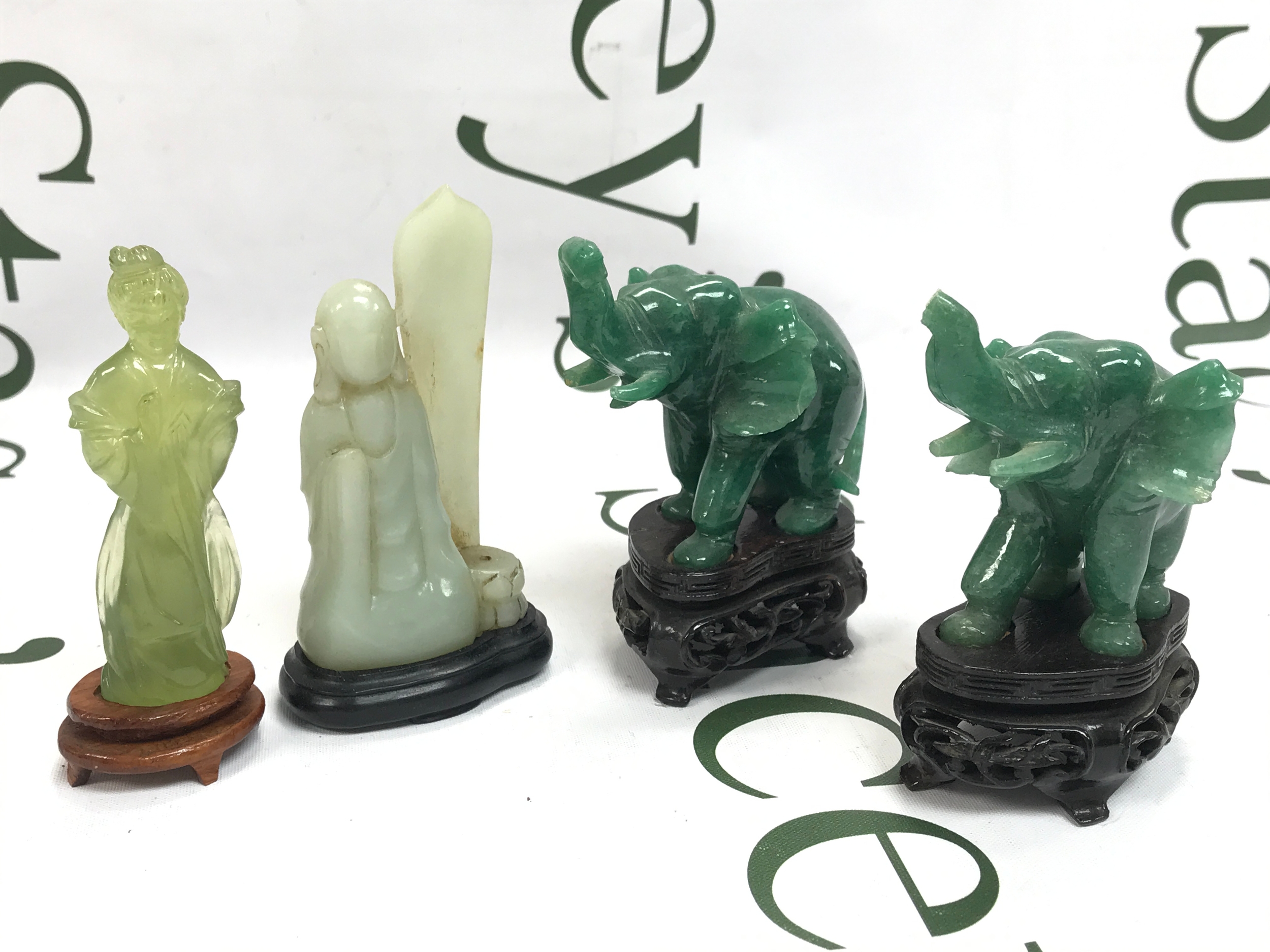 Carved green and white hardstone or jade-style Asian figurines, including two standing figures and two carved elephant statues with raised trunks on ornate wooden stands
