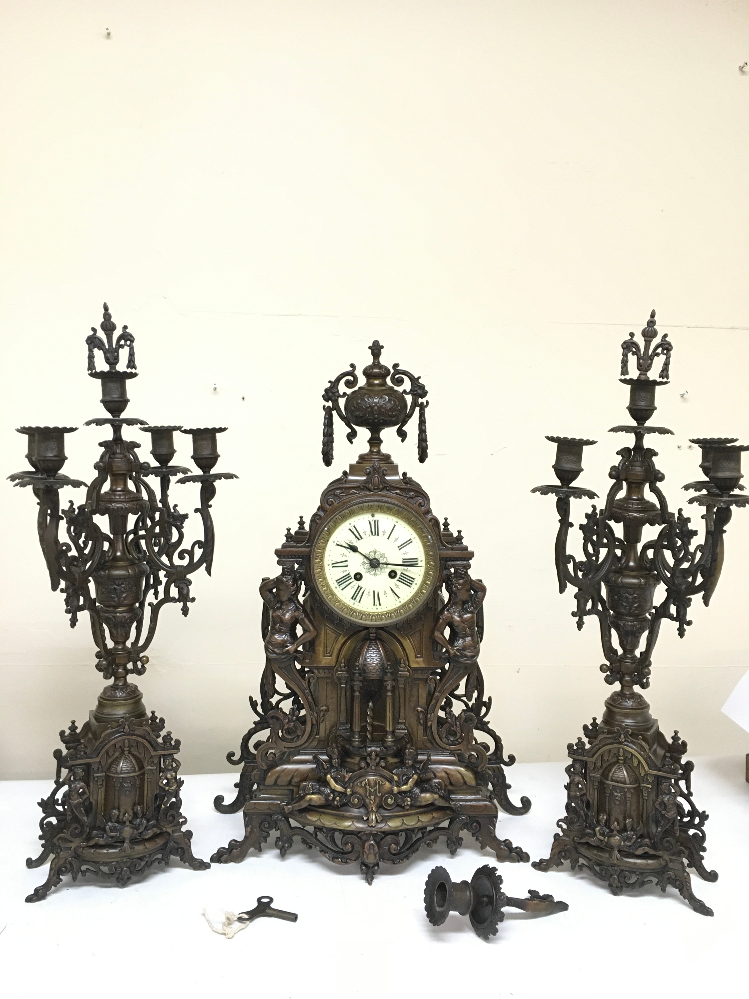 An Ornate Gothic revival architectural design clock featuring figural side details and intricate openwork metal (60cm tall), with candelabra garniture. broken piece (62cm tall). With key