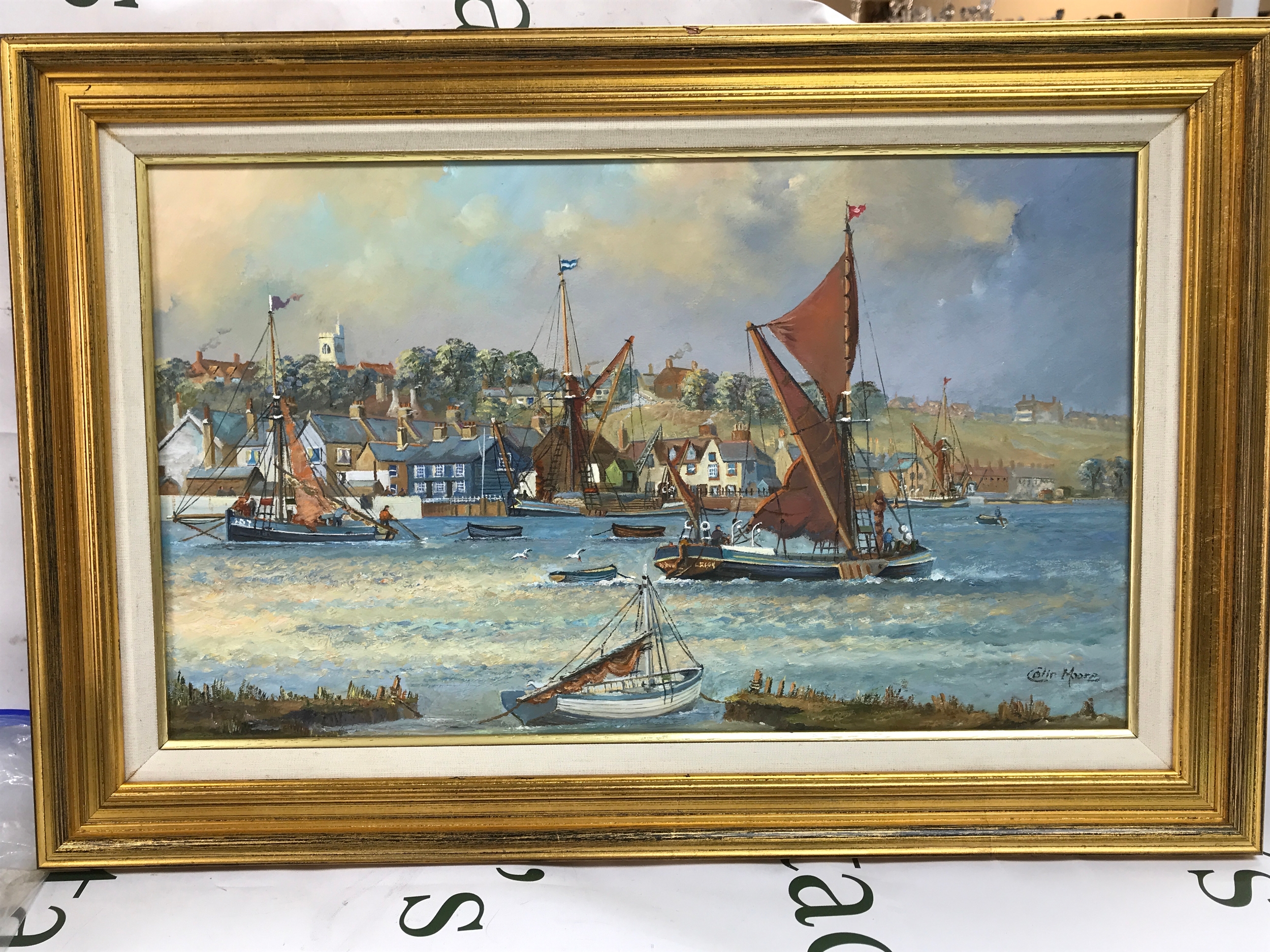 A framed Colin Moore watercolour, Thames barges at low tide with a waterfront background. 61cm wide 41cm tall 
