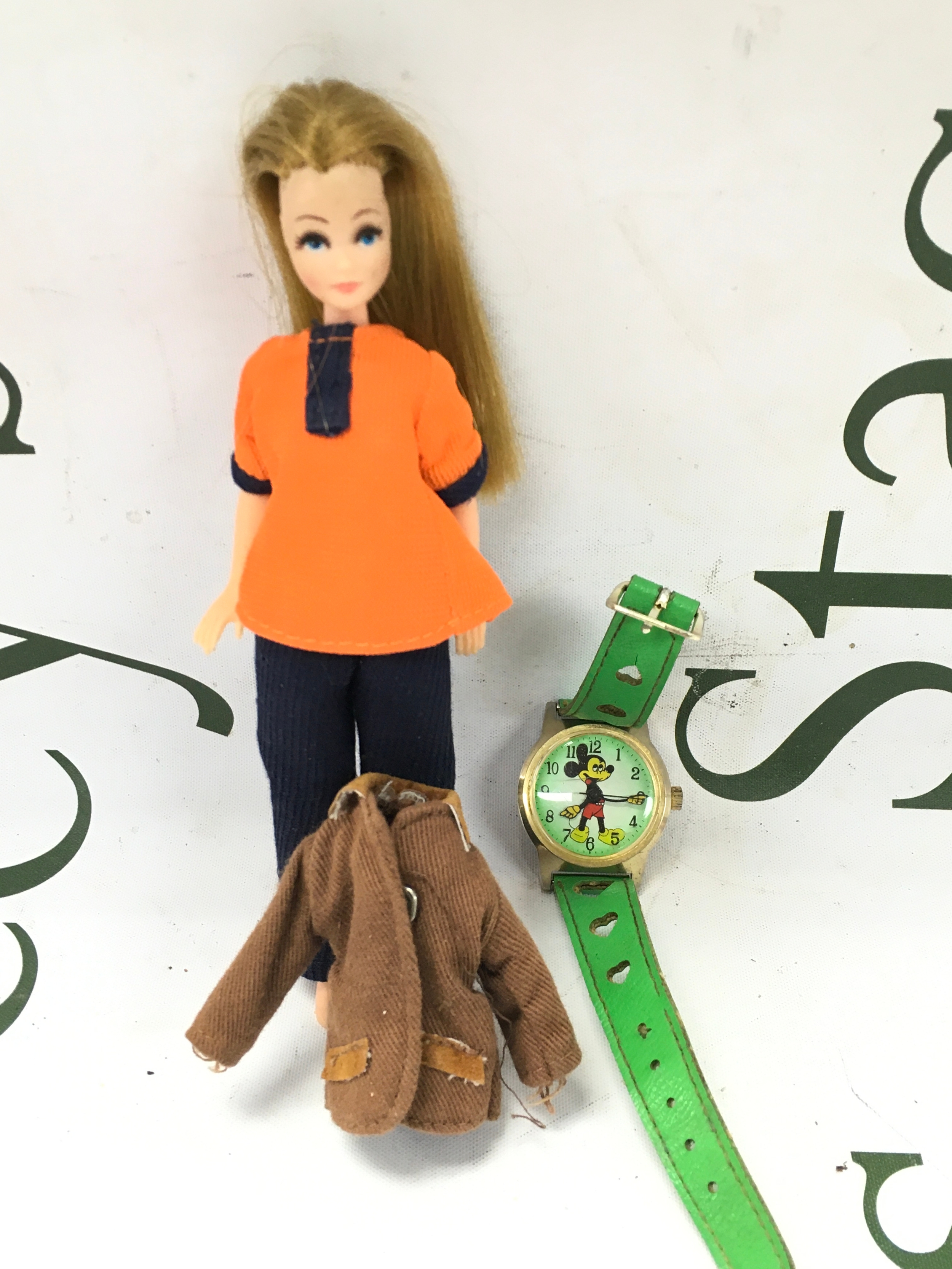 A vintage working manual wind Mikey Mouse watch with original green strap. And a vintage pipa doll, with jacket.