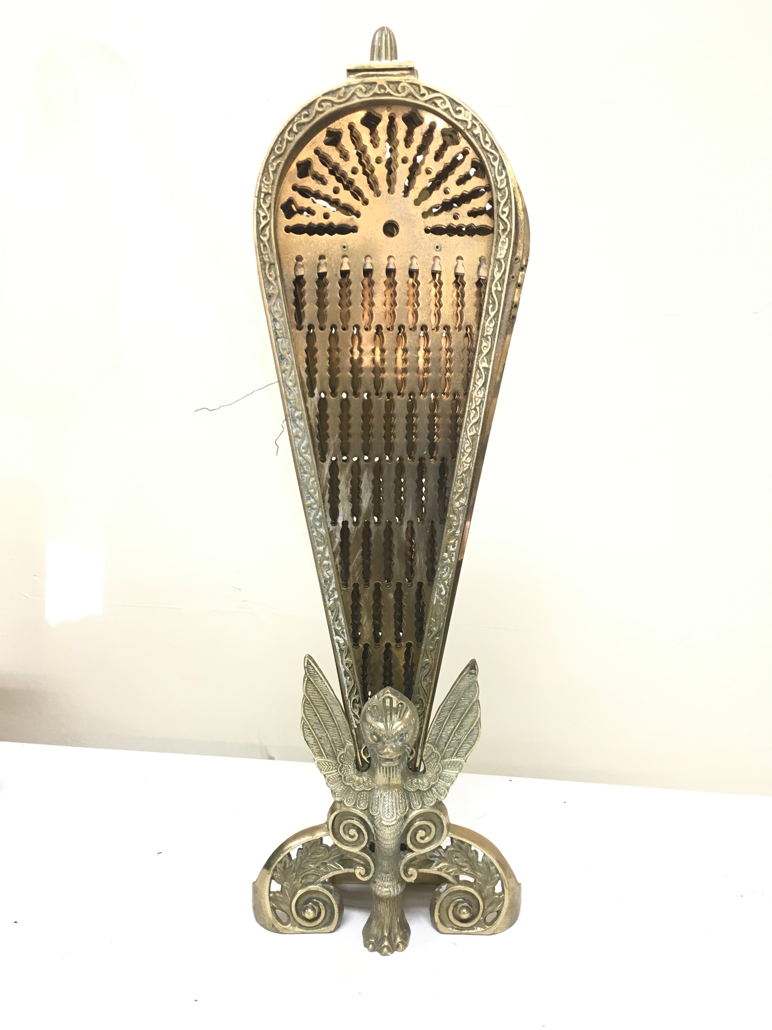 A vintage folding brass peacock fireplace screen featuring an ornate winged griffin base, 57cm tall