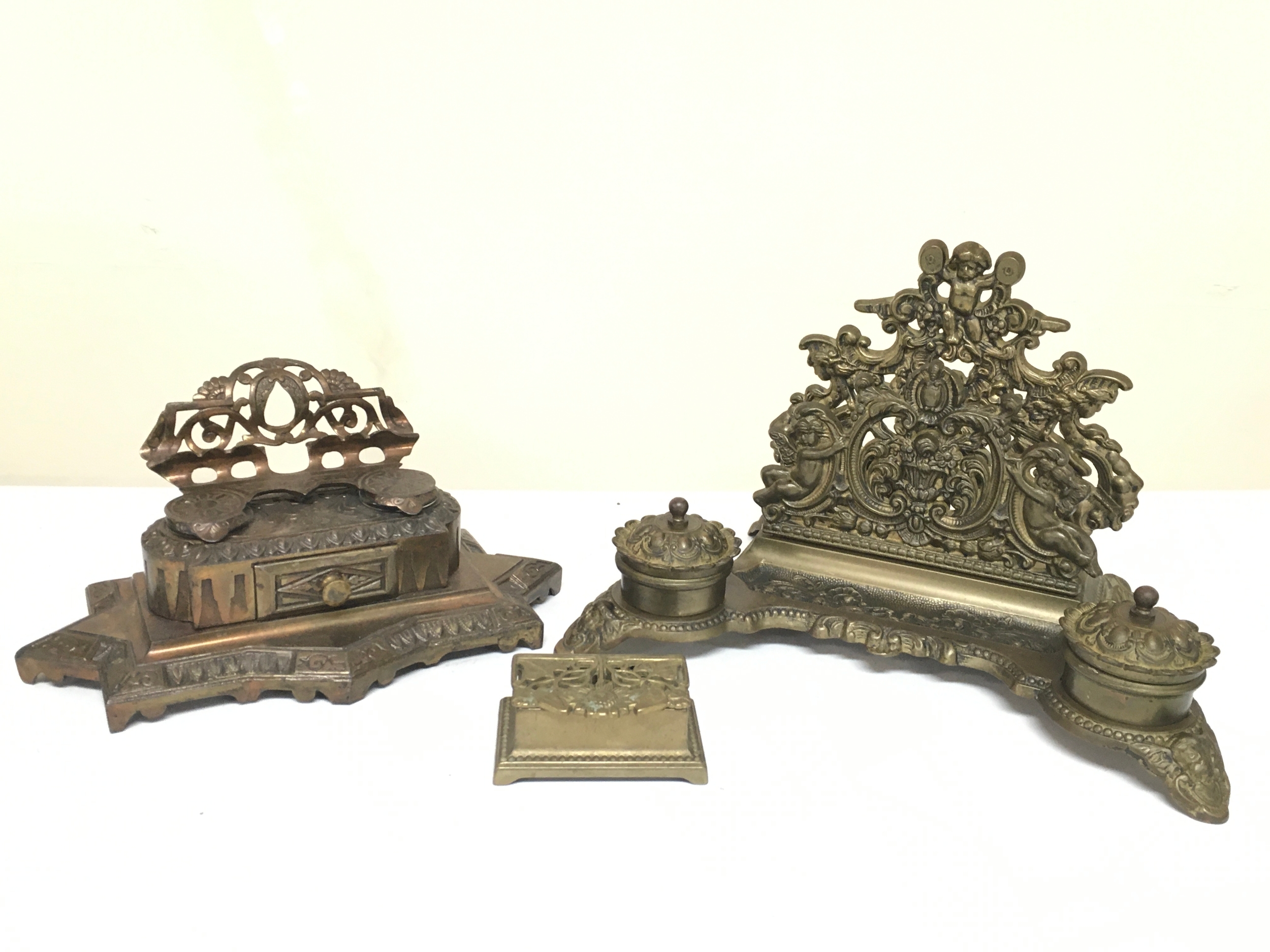 Two Brass desk sets featuring double inkwells and integrated letter racks, also a vintage cast brass stamp box featuring an Art Nouveau-style sunflower design and a hinged lid. 12 and 19cm tall, small box 4cm tall 