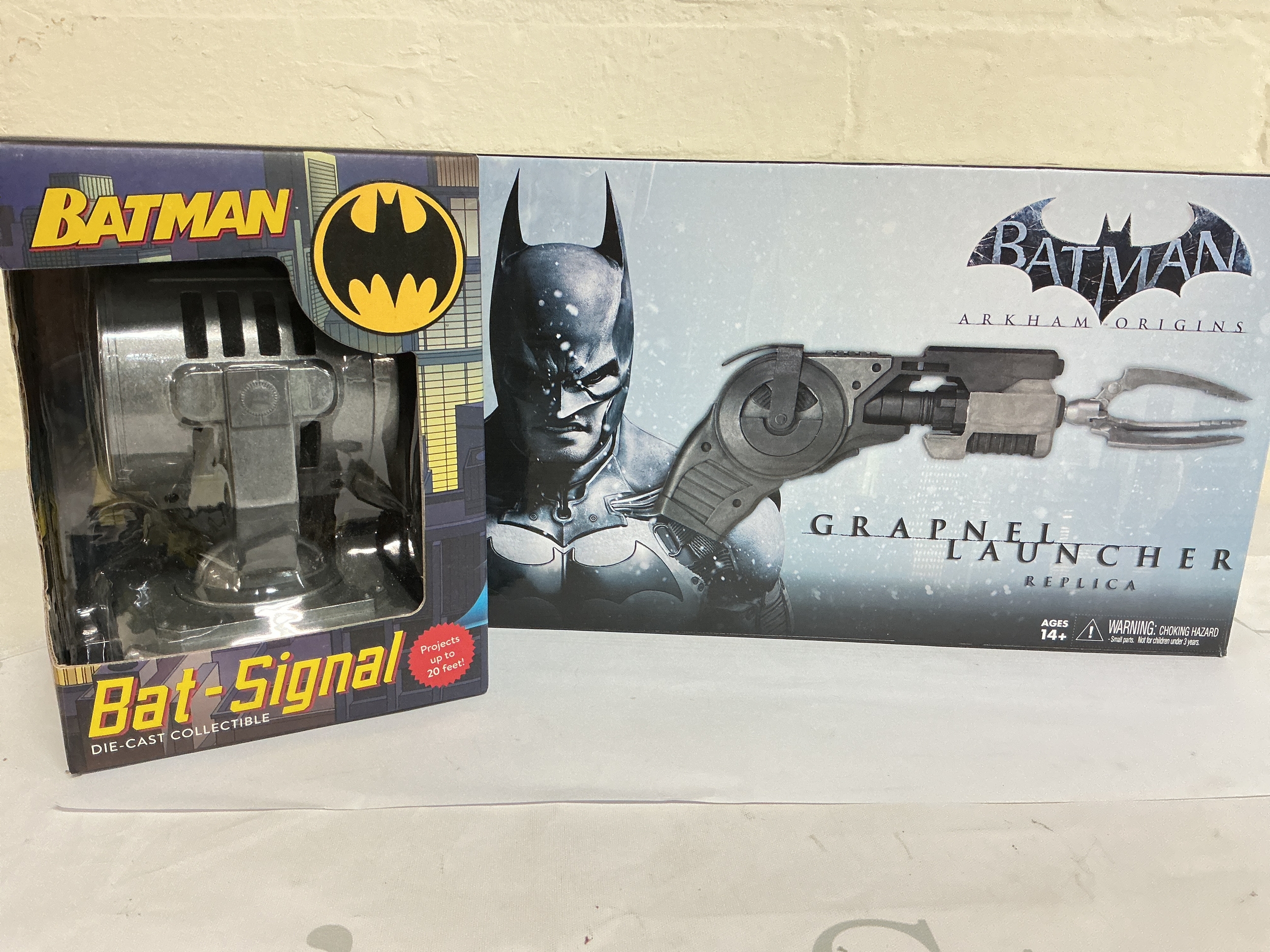 A Boxed DC Comics Diecast Bat Signal And A Arkham Originals Grapnel Launcher Replica.