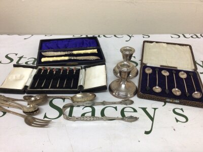 A collection of silver spoons sugar tongs cased silver coffee spoons a set of silver plated enamel cocktail sticks a pair of silver candle sticks loaded bases.