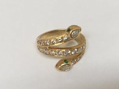 A high grade gold unmarked ring open crossover set with brilliant cut diamonds in the form of serpents with green emerald eyes. Ring size H.