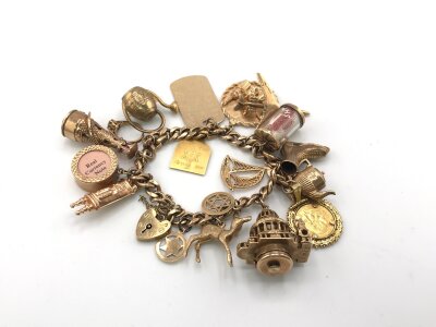 A large 9ct gold charm bracelet with various charms including an 18ct pendant and a Dos pesos coin.