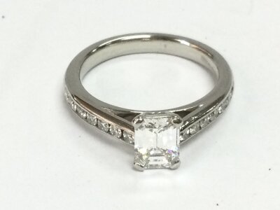A platinum diamond ring set with 0.85ct emerald cut diamond and smaller diamonds to the shoulders. Comes with GIA cert. 
Size J 1/2