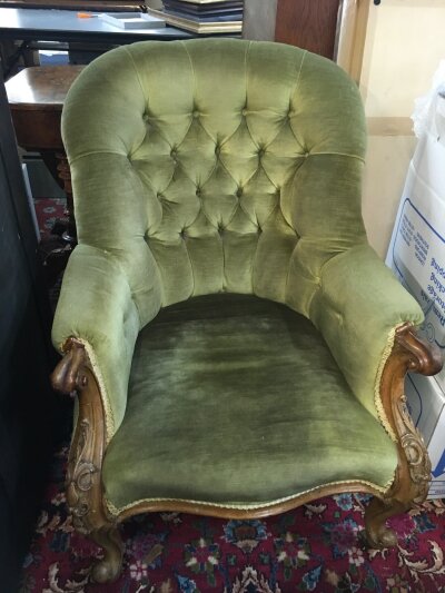 A Victorian armchair with carved design and green velvet upholstery.