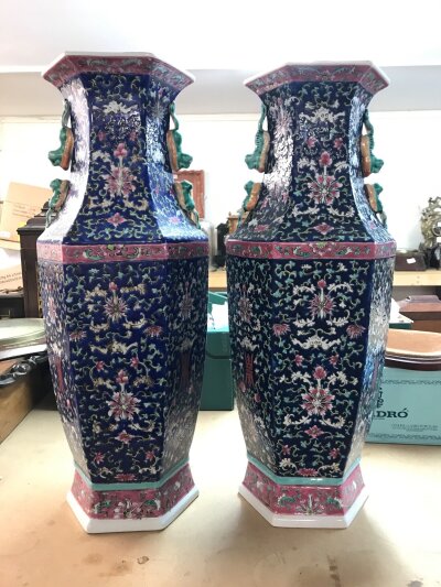 A pair of Chinese style blue ground porcelain vases , floral and butterfly motifs in a "famille rose" style, hexagonal in shape with relief-decorated foo dogs on the shoulders. 60cm tall