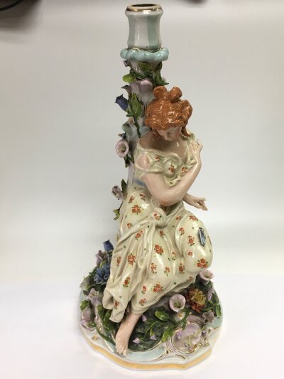 A German figural candlestick in the form of a maiden seated and surrounded by flowers, approx height 36.5cm. Some damage.