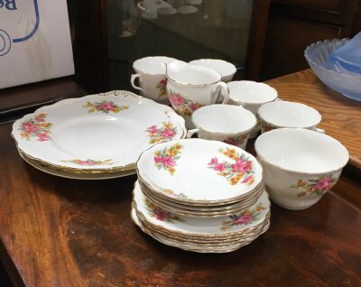 A ceramic tea set decorated with vibrant patterns featuring bright pink blossoms, clusters of small yellow flowers, and rich green foliage.