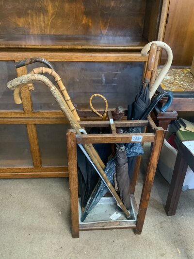 An 1930s oak stick stand with a collection of canes/sticks and umbrellas.