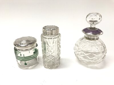 antique perfume bottle features a cut crystal body and a sterling silver lid with an amethyst coloured enamel accent along with two other silver topped glass items.