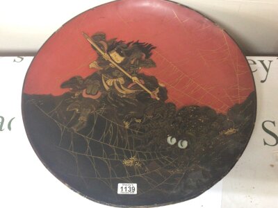 A large early 20th century Japanese lacquered paper mache dish decorated with a warrior slaying an Optus type creature with glass eyes some edge damage 52cm diameter.