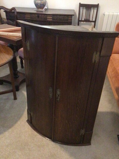 A George III oak bow fronted corner cabinet with dentil moulding above two doors with key.
