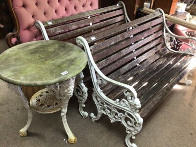 A Pair of traditional cast metal and slatted wood garden benches with raised lion masks and scrolls and a conforming wrought iron garden table possibly late 19th century with raised masks and an under tier. (3)