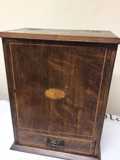 An inlaid oak smoker’s cabinet enclosing a tobacco jar above a drawer.