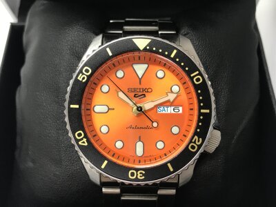 Seiko 5 Sport automatic watch featuring an orange dial and a stainless steel bracelet. Seen running with box and cards.