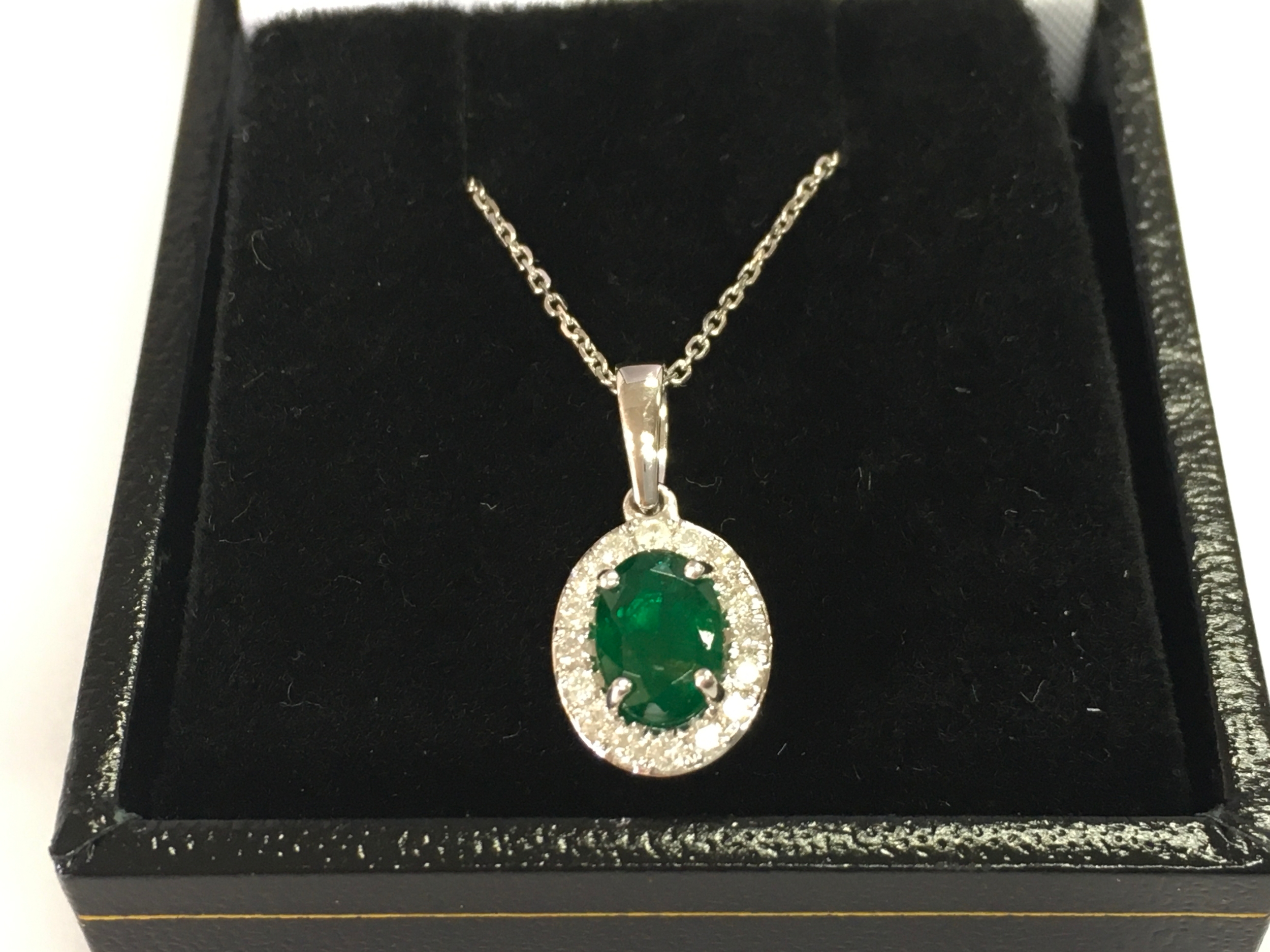 9ct white gold emerald and diamond cluster pendant on 9ct white gold chain. Emerald 0.76ct and 0.19ct diamonds.
