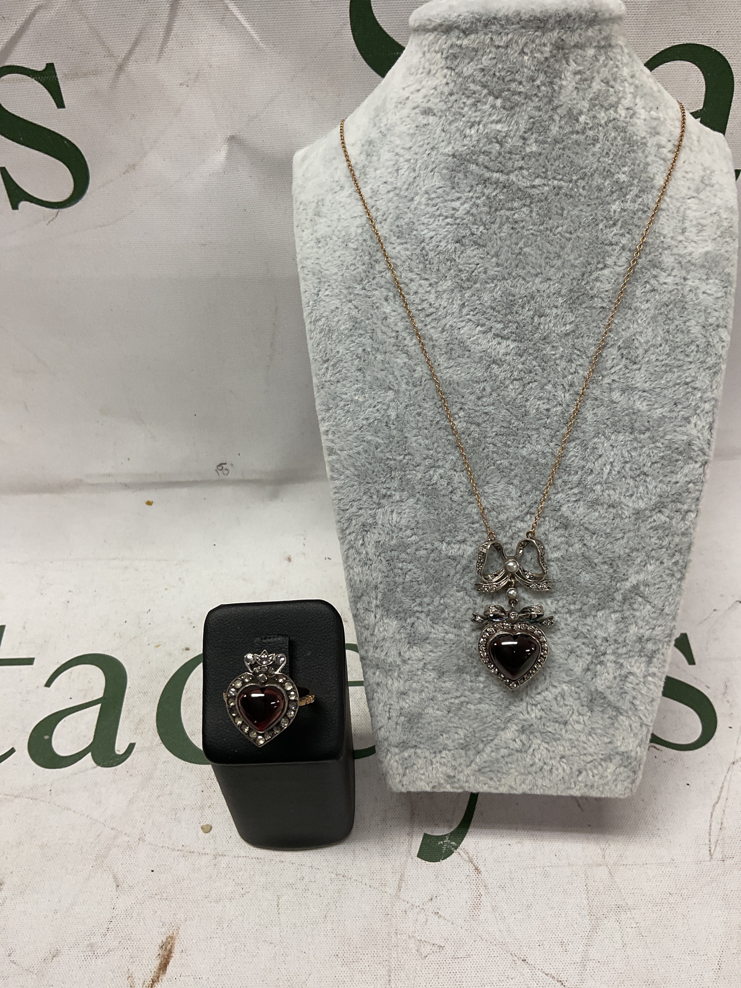 beautiful Diamond ribboned heart and crown ring and matching pendant on 9ct chain.the ring has the heart cabochon garnet to the centre with diamond surround surmounted by a crown set with diamonds, the necklace similar but set with additional seed pearls and ribbon swag to the top.comes in vintage leather box with Burlington Arcade addressed jeweller.