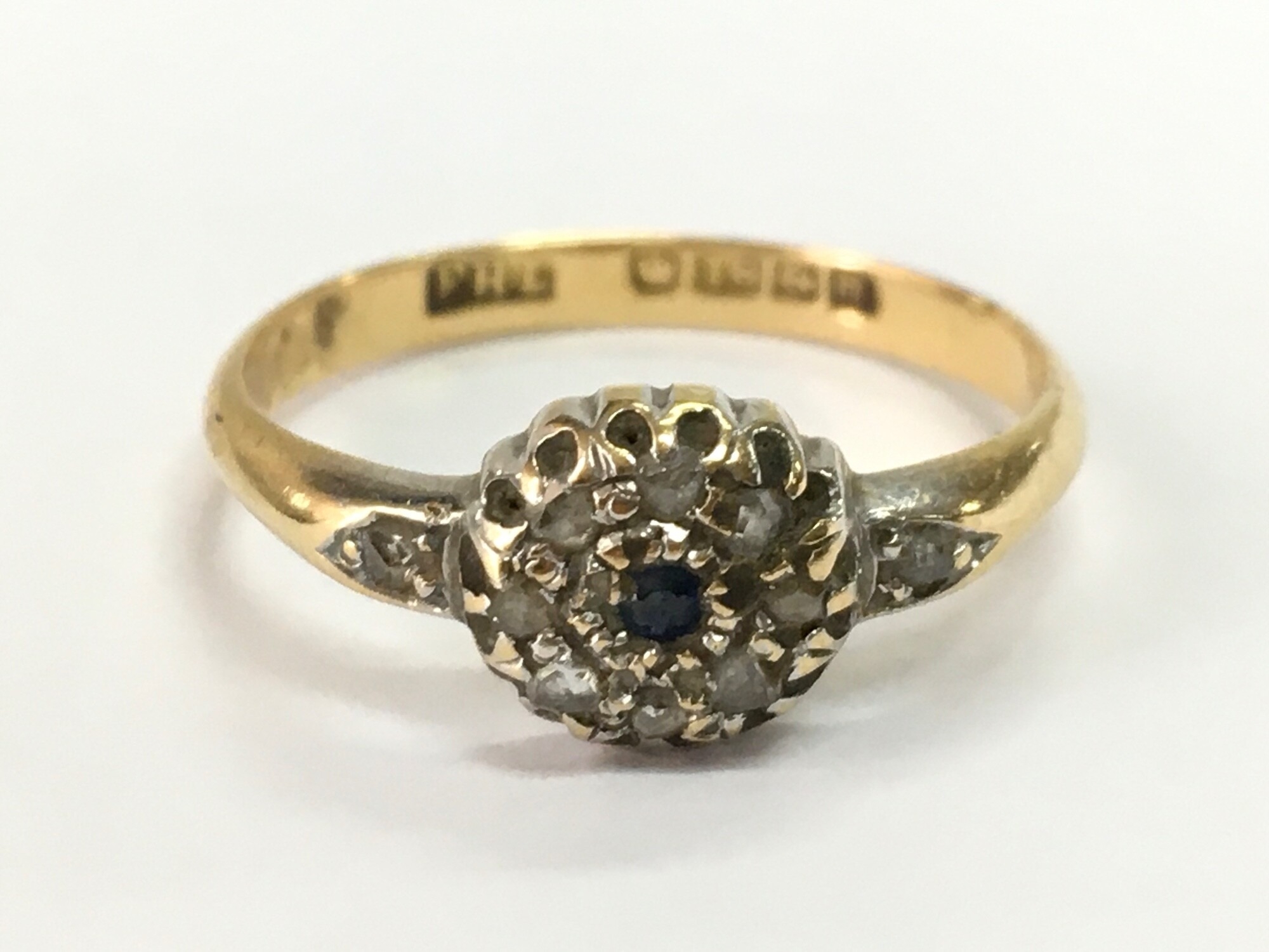 An 18ct gold ring set with a small sapphire surrounded by small diamond stones, size N. 2.6g total weight