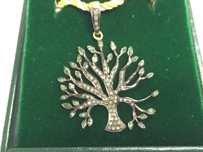 Silver gilt tree of life pendant with diamonds and tsavorite garnets on a woven material chain.