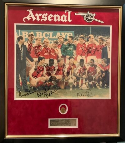 Arsenal 1988 - 1989 League Winners Signed Framed Football Photo: Stunningly framed team group of them celebrating after the famous win at Liverpool measuring 30 x 27 in its frame. Genuine autographs x 16 include Rocastle Adams Bould Merson and manager Graham. Replica gold plated medal displayed below photo. Full list on plaque under medal which is pictured online.