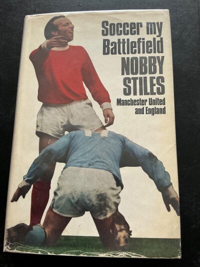 Nobby Stiles Manchester United + England Signed Football Book: Book named Soccer my Battlefield . Very good condition Stanley Paul book with dust jacket and undedicated autograph.