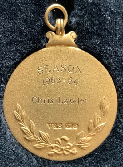 Liverpool 1963 - 1964 League Championship Winning Medal: 9ct gold medal awarded to Chris Lawler many years after playing 6 matches as a young lad in his first season for Liverpool. This medal is exactly the same as his team mates received in 1964 stating The Football League Champions Division 1 to front with reverse reading Season 1963-64 Chris Lawler with Vaughtons + Son stamp and hallmark. Whilst it was made by original maker Vaughtons the box states EFL. Dave Alexander dealt directly with the family and Chris enclosed the medal in an envelope which states To Dave Best Wishes Chris Lawler LFC which is included. Chris and a few other Liverpool players were awarded medals after the club thought it unfair they were not awarded a medal at the time as they did not make enough appearances.