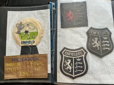 Enfield Football Memorabilia Folder: Unmissable folder with so much included many not available to the public. Includes itineraries for Amateur Cup finals 64 82 + 88, programmes with tickets, 1967 Amateur Cup final replay ticket, armband for presentations, tours to 1956 1957 + 1959, rosettes, old shirt badges and so much more.