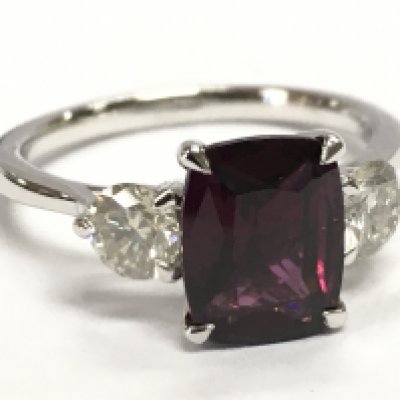 A platinum three stone ring set with a cushion step-cut almandine garnet and 2 RBC diamonds. Garnet 2.36ct, diamonds 0.63ct. Size N.