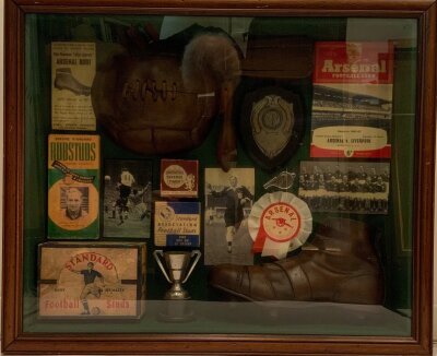 Arsenal Football Memorabilia and Ephemera Display: Nicely framed box featuring rattle, football boot, referees whistle, studs, lace up football and more. Unusual item with box measuring approximately 61x51x11cm.