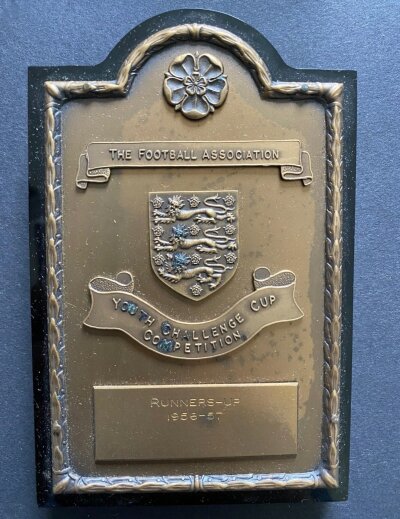 1957 John Lyalls West Ham Youth Cup Final Plaque: Attractive shield in original box engraved J Lyall. West Ham were runners up after losing the two legged final to Manchester United. Lyalls own poor condition home programme included.