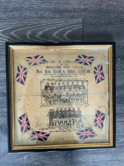 1923 FA Cup Final Bolton v West Ham Napkin: Stunning 103 year old original napkin that was on the table at the first match at Wembley for dignitaries. Surrounded by the Union Jack is team groups of both teams all named underneath, details of the match and information that the King arrives at 2.45pm. Whilst it had damage it is now framed and is an attractive item.