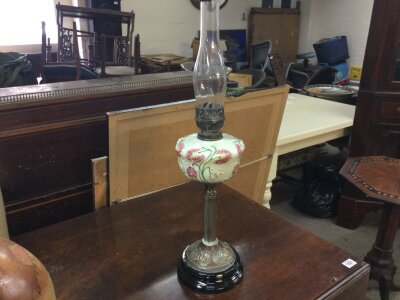 An oil lamp featuring a hand-painted floral glass font, a brass burner, and a clear glass chimney. 70cm tall