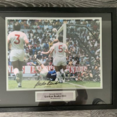 Gordon Banks Greatest Save Signed Framed Photo: Lovely colour photo taken from a side angle of Banks somehow saving from Peles header in the 1970 World Cup. Hand signed with photo proof COA to rear. Measures 21 x 17 inches.