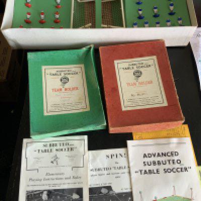 Subbuteto Football Games: 1964 Super Set which is believed to be complete of everything with rules etc. C/W two empty team holders in below average condition in green and red. C/W Emlyn Hughes Soccer Management Game and mug and keyring set.