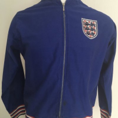 Bobby Moore England Football Tracksuit Top: Umbro top in blue with red and white trim to neck and cuffs. England stitched to rear. Letter of provenance from original vendor is pictured online and states that it was given by Bobby to Mrs Corbett who was a cleaner at Wembley. It came to vendor in a house clearance framed with a magazine picture of Bobby wearing this style top. Now removed from frame with no damage. The make up of this top is correct for around 1970 with embroidery and labelling the same as previous similar items we have had direct from players over the years.
