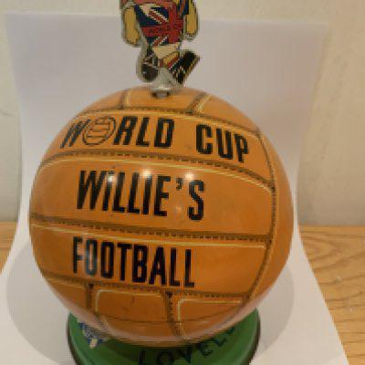 1966 Football World Cup Willie Toffee Tin: Lovells football shaped metal tin with FA 1965 to base. Top which lifts off states World Cup Willies Football. WC Willie is never intact as kids used him to pull lid open but he is present and can be stuck back.