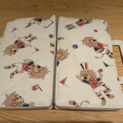 1966 World Cup Willie Seat Cushion: Folded cushion used to pad the wooden Wembley Stadium seats at the World Cup. Intended to be carried into the stadium with handle intact.