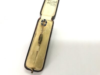 A vintage tin pin in horse shoe design set with blue and white stone.