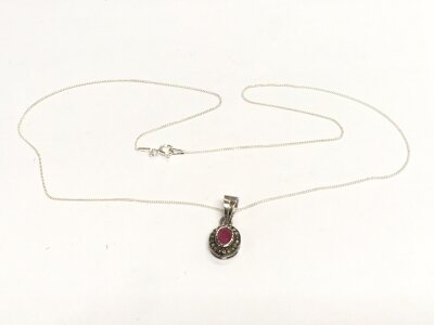 A silver pendant set with an oval ruby surrounded by diamond chips. Ruby approx 0.40ct, diamonds approx 0.18ct.