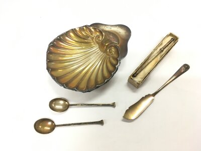 A small collection of silver including a dish in the form of a shell, two coffee spoons, butter knife and a swizzle stick.