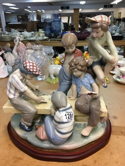 A large Lladro figure group of young boys playing cards on a bench. 30cm in height, not including wooden base