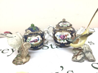 Two Royal Worcester type tea pots decorated with panels of birds on a scale blue ground some damage and two ceramic bird ornaments a Beswick Lesser Spotted woodpecker and one other continental bird ornament. (4)