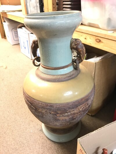 A large Chinese ceramic vase featuring a celadon glazed neck and base, with a central mustard-colored band decorated with a low-relief scene of figures in a landscape. 65cm tall