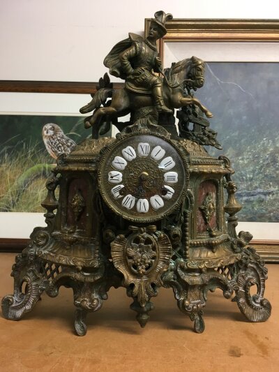 A gilt metal mantle clock ,of classical influence- surmounted with horse and rider- the circular dial having Roman numerals.  40cm in height