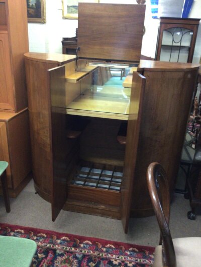 An Art Deco Walnut and satinwood Cocktail cabinet of semi circular shape with a mirrored and fitted interior flanked by cupboards.