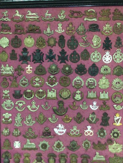 A framed collection of I world war and other British Military Regimental hat badges.